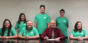 DeKalb County Mayor Tim Stribling signs a proclamation to declare that June is Dairy Month. Front: Jenna Cantrell, Elizabeth Seber, Tim Stribling, & Ansley Cantrell. Back: Laura Magness, Colby Barnes, and Luke Magness.