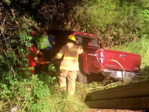 County Fire Chief Donny Green and other Firefighters and EMS personnel access truck after it was pulled away from a tree where it came to rest on its side