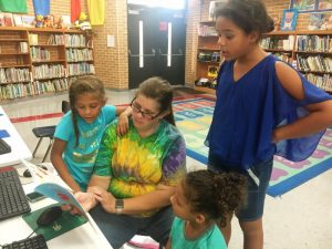 Rebecca Waggoner reading with children Mekazya Waggoner (left), Kynsley Hamilton (right), and Jakayta Odom (taller girl) at Smithville Elementary School