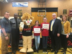 D.A.R.E. Essay winners recognized during D.A.R.E graduation ceremony at DeKalb West School Monday. Pictured: Detective Billy Tiner, D.A.R.E Instructor and DWS SRO officer Lewis Carrick, DAREN the Lion (D.A.R.E Mascot) Essay winners Hannah Brown from Jeanna Caplinger’s class and Kenadee Prichard (Overall Winner)from Nadina Martel’s class, Judge Bratten Cook, II who presented a $50 check to Kenadee, and DWS Principal Sabrina Farler.