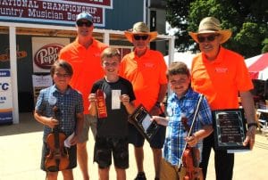 Finley Reed of Normandy Tennessee earned the top Jamboree award as the best fiddler in the National Championship for Country Musician Beginners. Finley Reed (pictured front right holding fiddle) won the coveted James G. “Bobo” Driver Memorial Award, named for the man who started the children’s competition as part of the annual Fiddler’s Jamboree and Crafts Festival. Members of Mr. Driver’s family presented the award to Reed including (pictured left to right in back dressed in orange) Adam Driver, Bobo’s grandson; and sons Jimmy and Mickey Driver. Also pictured in front Beginner Fiddle contestants Deacon Collier of Gallatin (3rd Place Far Left) and Ace Walters of Lebanon (Center-2nd place)