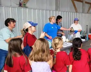 Third graders learn how to make homemade butter from Farm Bureau Board Member Jana Crook, 4-H Agent Brooklyn Gunter, and 4-H members Sydney Polk and Ari Dodds.